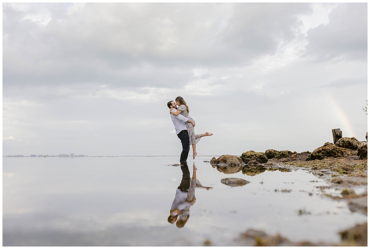 Couple with rainbow in the background embracing - Dreamy miami engagement ocean photoshoot